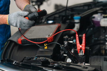 Fototapeta na wymiar Electric vehicle car battery repair service Automotive mechanic testing car battery with red jumper cable and diagnostic tool