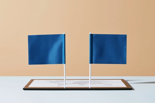 Two blue fabric desk flags facing each other over a digital map on a polished surface, reflecting a diplomatic meeting with ample copy space