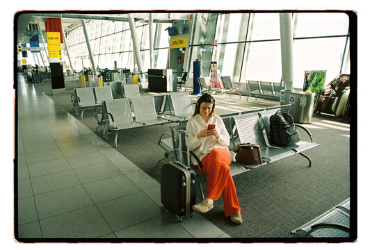 A woman scrolls her phone in an airport departure hall