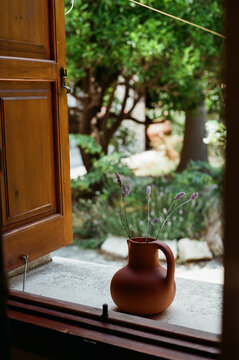 Clay Pot With Flowers on a Windowsill With Greenery Outside