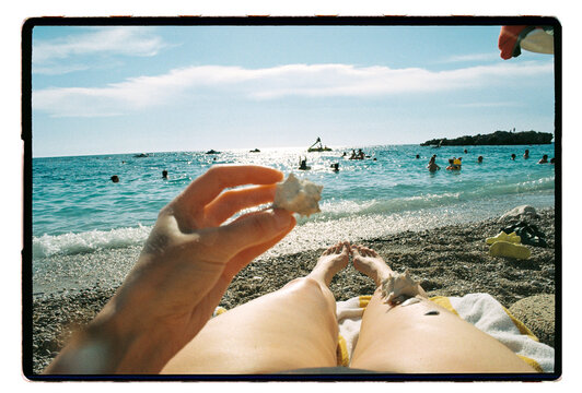 A woman holds a seashell up from a sun-warmed pebble beach