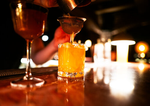 A bartender pours a cocktail in a speakeasy bar.