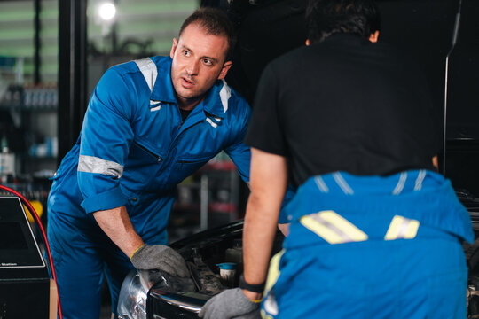 Mechanic repairing vehicle in workshop with focused teamwork and blue protective uniform