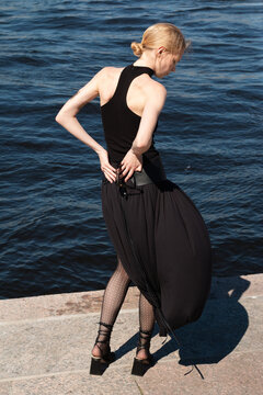 A young woman in black outfit looking at dark blue water.