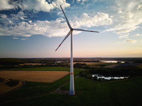 Wind Turbine Stands in a Field Near a Lake During Sunset