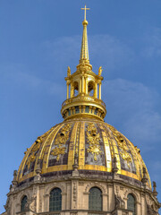 Fototapeta premium The gilded dome of Les Invalides gleams against a brilliant blue Parisian sky, its ornate golden lantern and cross crowning this iconic Baroque masterpiece.