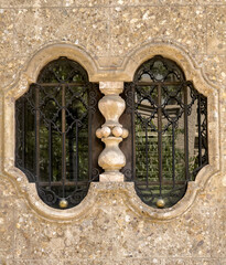 A twin arched window with ornate wrought-iron grilles, divided by a carved stone balustrade column, set into a textured pebble-dash facade. © Dan Van Pelt