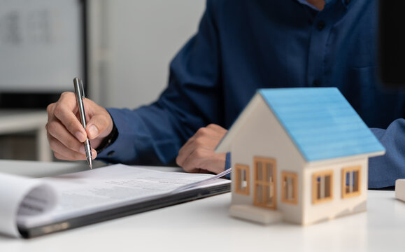 Businessman reviewing home loan documents beside house model, representing mortgage application, real estate contract, property financing, home purchase, loan approval and ownership planning.