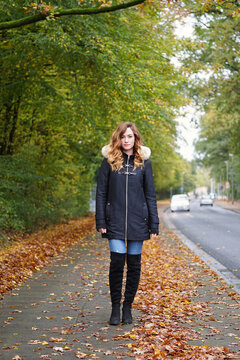 Young woman walking on sidewalk covered with autumn leaves next to street in Germany