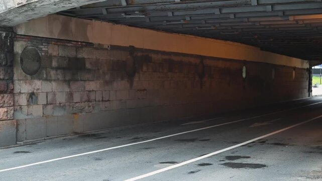 An underpass shows a small roadway with faded markings and a rough concrete surface. The structure has a dark ceiling and visible pipes along the walls