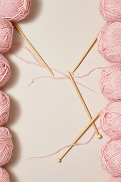 Pink background with balls of soft knitting yarn and wooden needles framing a central copy space for craft and hobby campaigns