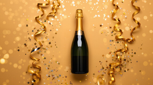 Champagne bottle with confetti stars, bokeh decoration and party streamers on golden background. Christmas, birthday or wedding concept. Flat lay.
