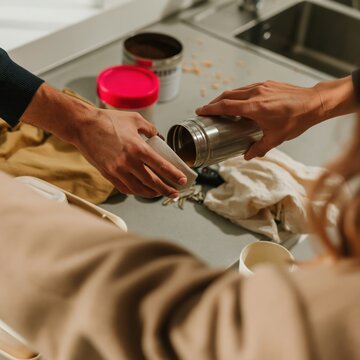 Reusable travel mug being filled with a hot drink on a grey countertop, steaming and ready for a morning commute, with copy space for coffee brands