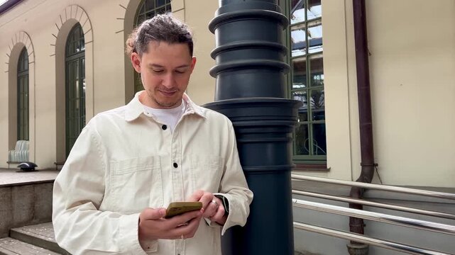 Middle aged man waiting on railway platform, thoughtfully scrolling through his smartphone while waiting for train in slow motion 4K footage. Train travel, digital communication and waiting concept