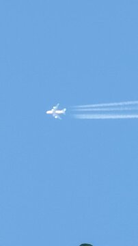 A widebody four-engine commercial aircraft cruising at high altitude across a clear blue sky with visible white vapor trails and contrails against a cloudless sky background.