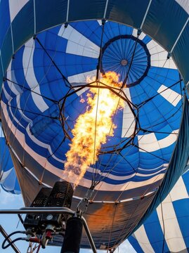 Close-up View of a Hot Air Balloon Burner Firing a Powerful Orange Flame into the Blue and White Envelope