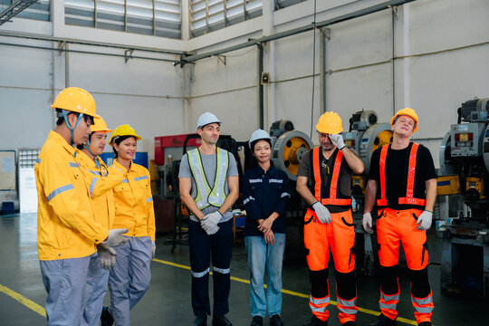 Diverse factory team members share joyful moment in busy industry as engineers communicate with happy faces inside building