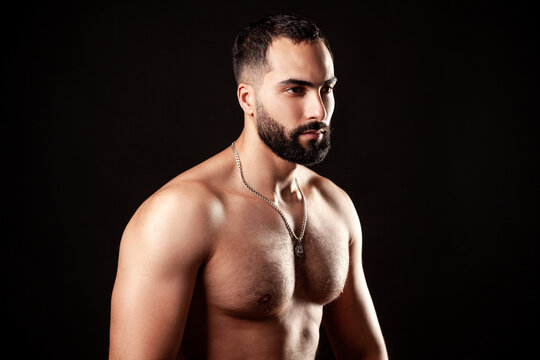 Shirtless athletic man with detailed muscular chest and shoulders in three-quarter view with silver necklace and intense expression in soft studio lighting isolated over black background
