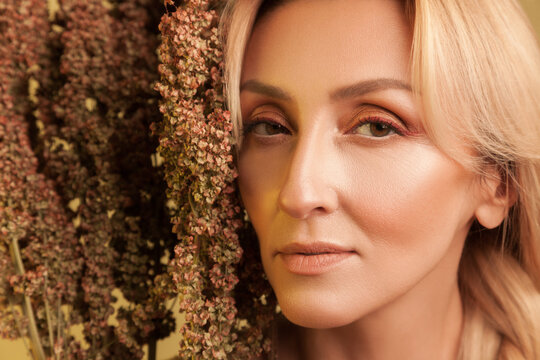 Intense gaze of blonde woman behind autumn vegetation looking straight at camera and showing perfect skin isolated over yellow background