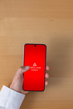 Top view of hand holding smartphone with security alert message on screen over wooden desk