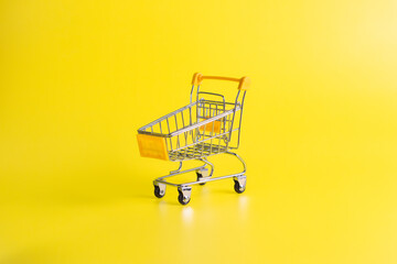 Yellow miniature shopping cart on a solid yellow background. Concept of retail commerce, online shopping, and consumerism.  © wibiwisnu