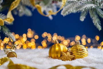 Naklejka premium A Christmas background featuring an abundant array of gold baubles, an ornate filigree ornament, and a star wrapped in ribbon on snow, set against deep blue with twinkling lights and copy space.