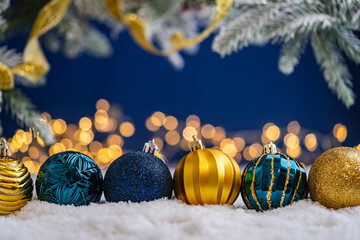 Naklejka premium A Christmas background featuring a row of teal and navy baubles with etched patterns and gold accents on snow, framed by frosted pine and gold ribbon, set against deep blue with lights.
