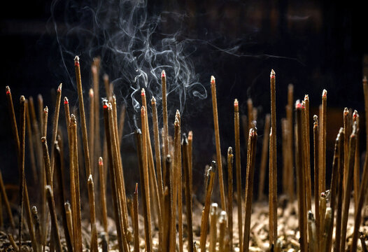 Burning incense sticks with rising smoke in a dark temple setting for spiritual rituals and meditation
