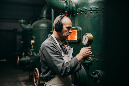 Veteran boiler operator checking a pressure gauge on an industrial furnace with a glowing firebox