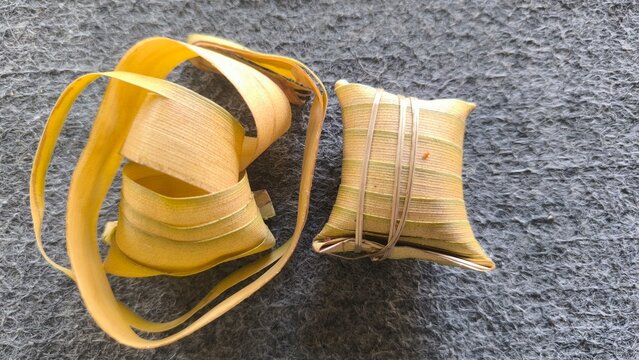 Traditional Sundanese leupeut food wrapped in woven young coconut leaves, showcasing a traditional Indonesian food preparation technique on a textured background.