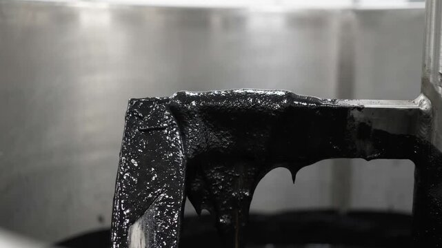 heavy steel mixing paddle rotating horizontally and folding viscous black graphite slurry over its thick black coated metal surface