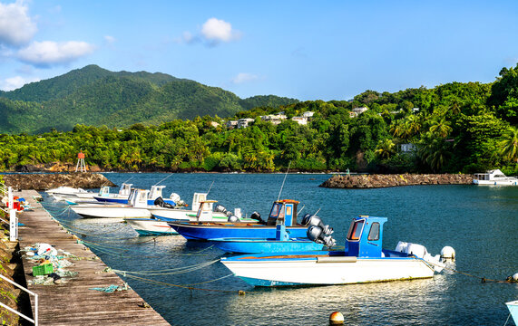 Small motorboats moored along a wooden pier in Port de Trois-Rivieres, surrounded by lush tropical hills in Guadeloupe, Caribbean France