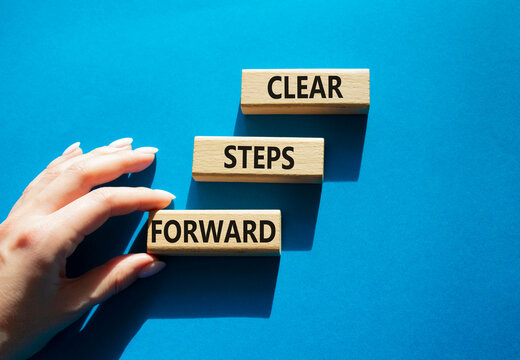 Clear steps forward symbol. Concept words clear steps forward on wooden blocks arranged as steps. Businessman hand arranging wooden blocks. Progress and planning concept. Blue background. Copy space.