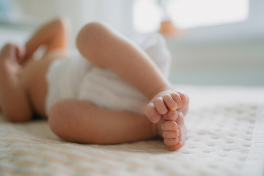 Baby lying on a soft changing pad wearing a breathable eco friendly reusable cloth diaper, showcasing tiny feet and legs, emphasizing sustainable and gentle hygiene for newborns