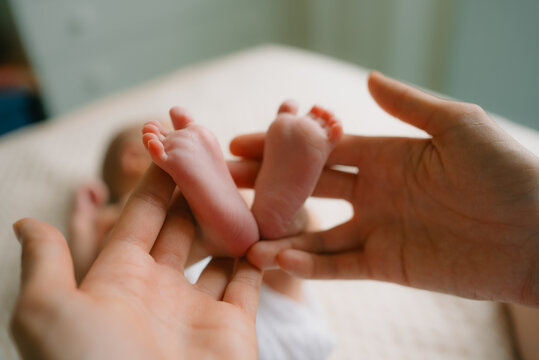 Mother's hands tenderly supporting newborn baby boy's small feet, representing the, protection, and nurturing care parents provide for their infant