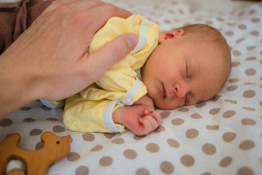 Parent hand gently resting on a newborn baby sleeping soundly in a crib, symbolizing protection, care, and the beginning of new life with parental love