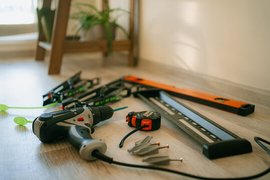 Tools and hardware for tv installation spread on a light wooden floor, power drill, measuring tape, spirit level, wall plugs and mounting bracket components ready for diy setup