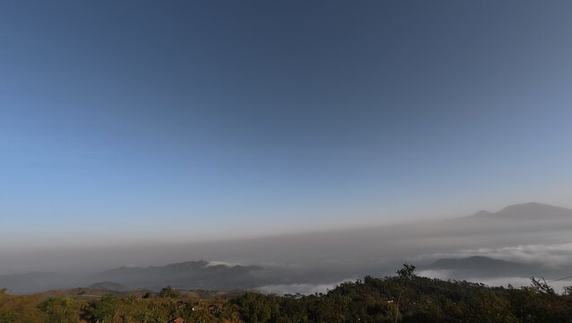 Panoramic view of morning mist rolling over tropical hills under clear blue sky