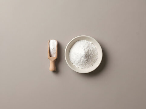 Creatina powder in a small ceramic bowl and a wooden scoop on a neutral beige background top view