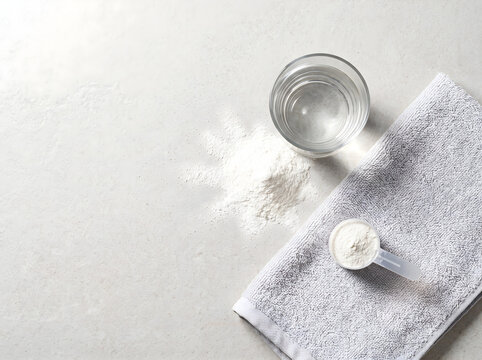 Flat lay composition with a scoop of creatina powder, a glass of water and a gray towel on a table