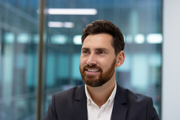 Fototapeta premium Close-up photo of a smiling young male businessman in the office, looking to the side