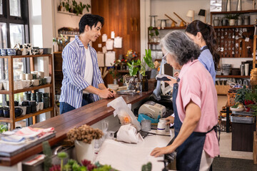 A customer stands at the counter of a retail shop to pay for items while a group of staff members helps process the transaction inside the store with wooden shelves. © winnievinzence
