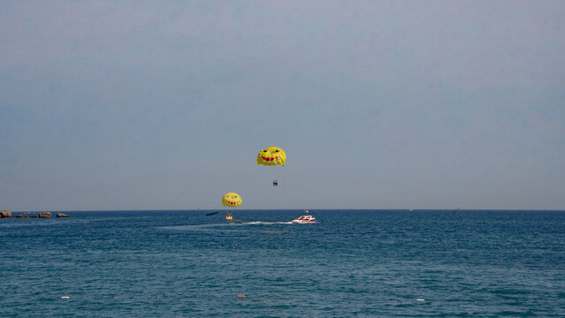 Two colorful parasails soar above the tranquil blue ocean, creating a fun and adventurous atmosphere.