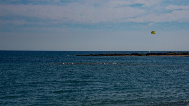 A vibrant seaside view showcasing the tranquil ocean under a clear blue sky with a lone parasailer above the water.