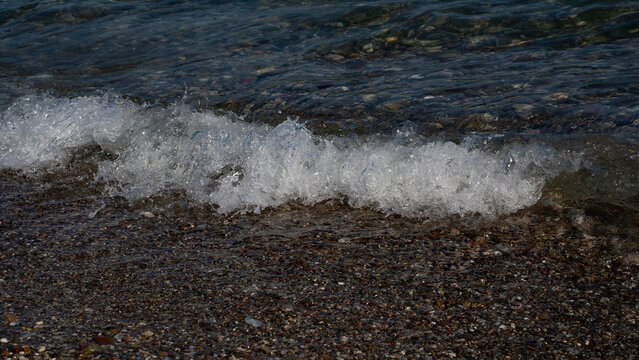A gentle wave crashing onto a pebbly beach, creating a serene and refreshing seaside ambiance.