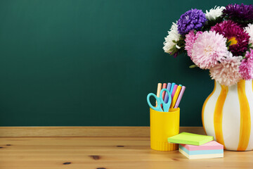 Different stationery and beautiful flowers on wooden table near chalkboard. Space for text © New Africa