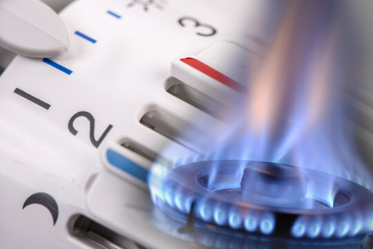  Eine Gasflamme brennt vor dem Thermostat einer Heizung - FOTOMONTAGE