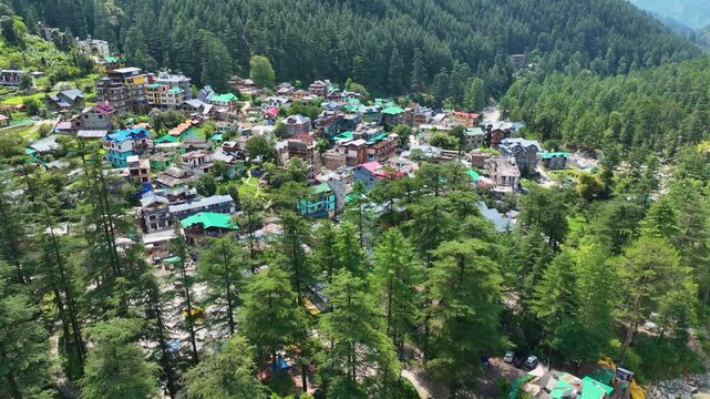 High angle drone tracking shot ascending past lush alpine treetops revealing Kasol town nestled in the Parvati Valley, a prime tourism destination in Himachal Pradesh, India.