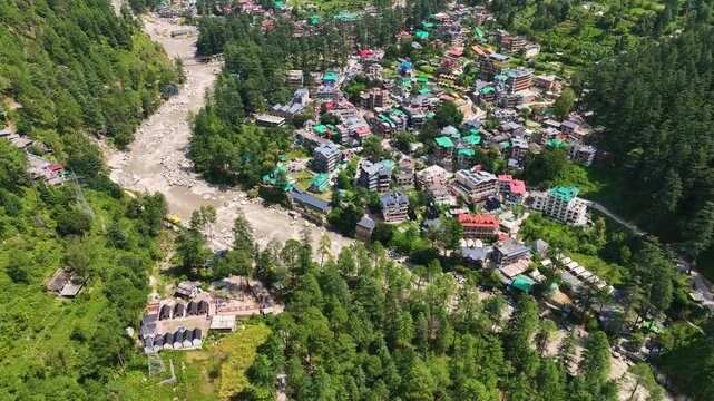 Cinematic drone establishing shot of the Parvati River Valley with Kasol town and lush Deodar cedar forests in Himachal Pradesh India