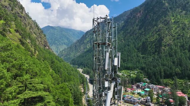 Drone view orbiting a high-altitude telecom tower above an off-grid village, illustrating the encroachment of human infrastructure into pristine mountain terrain.